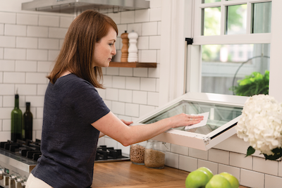 Single hung tilt A woman with red hair and a navy shirt cleaning the outside of a single-hung window bottom sash in a kitchen window.