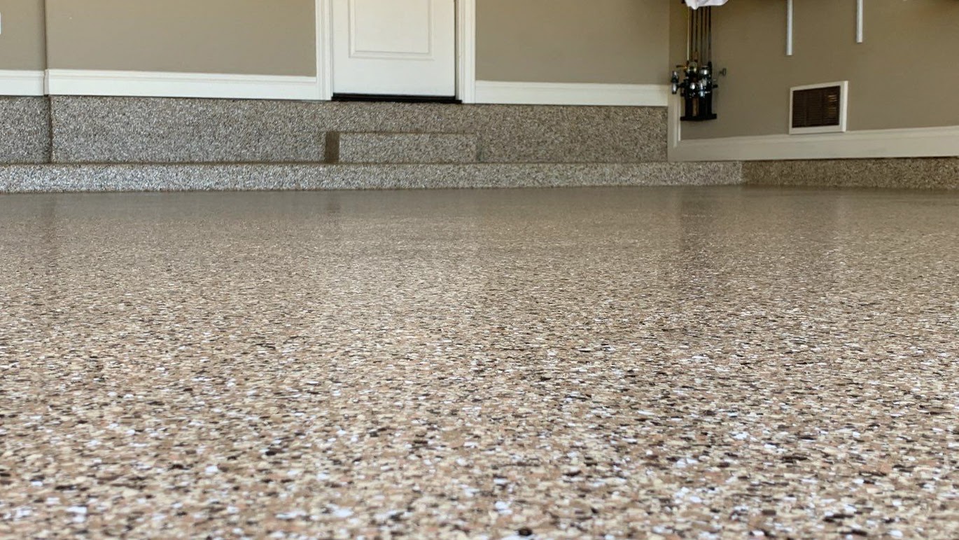 A up close photo of a garage floor coated with small flakes of beige, black, and white to look rock-like.